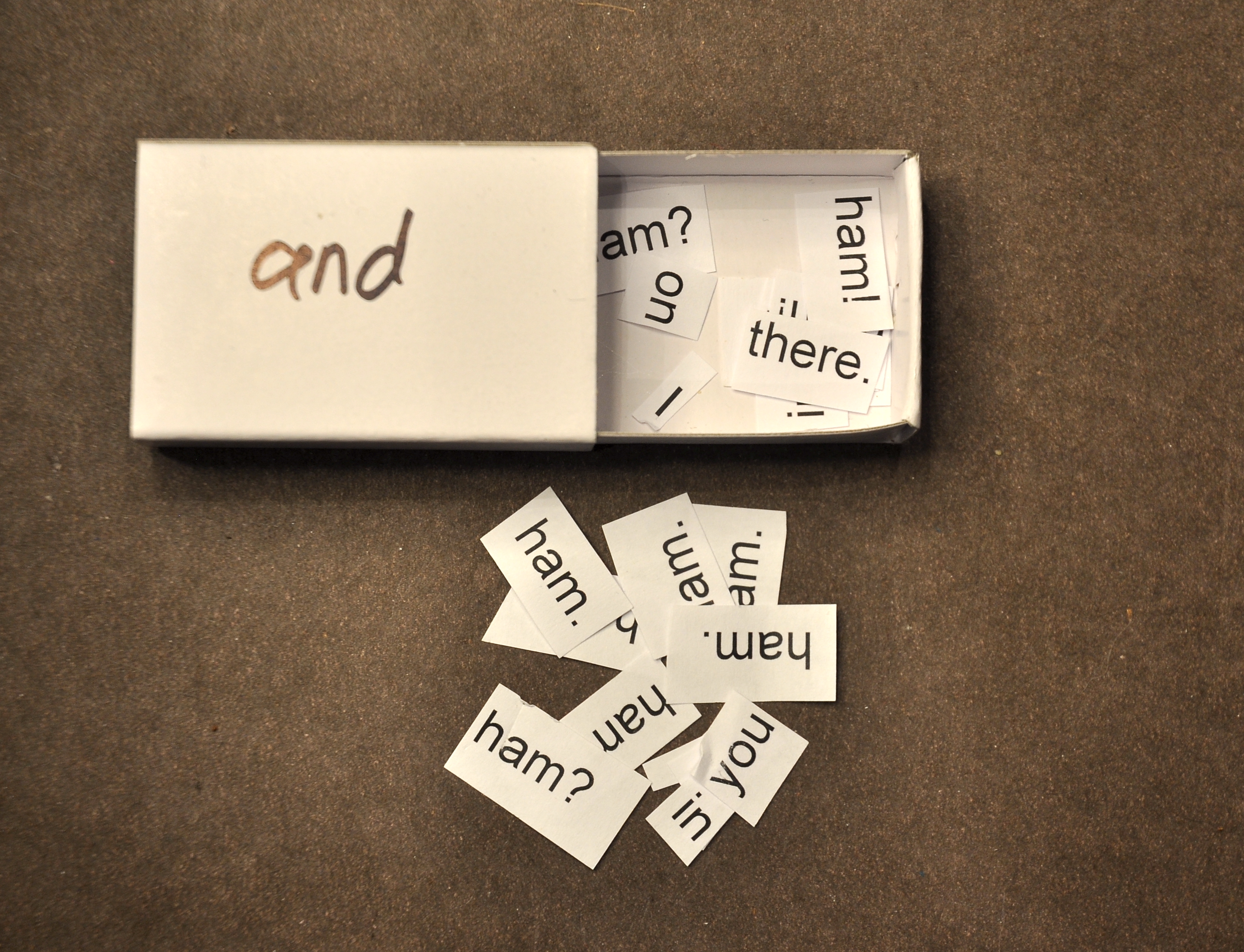 a matchbox with the word 'and' written on top, open to show the word many words on slips of paper